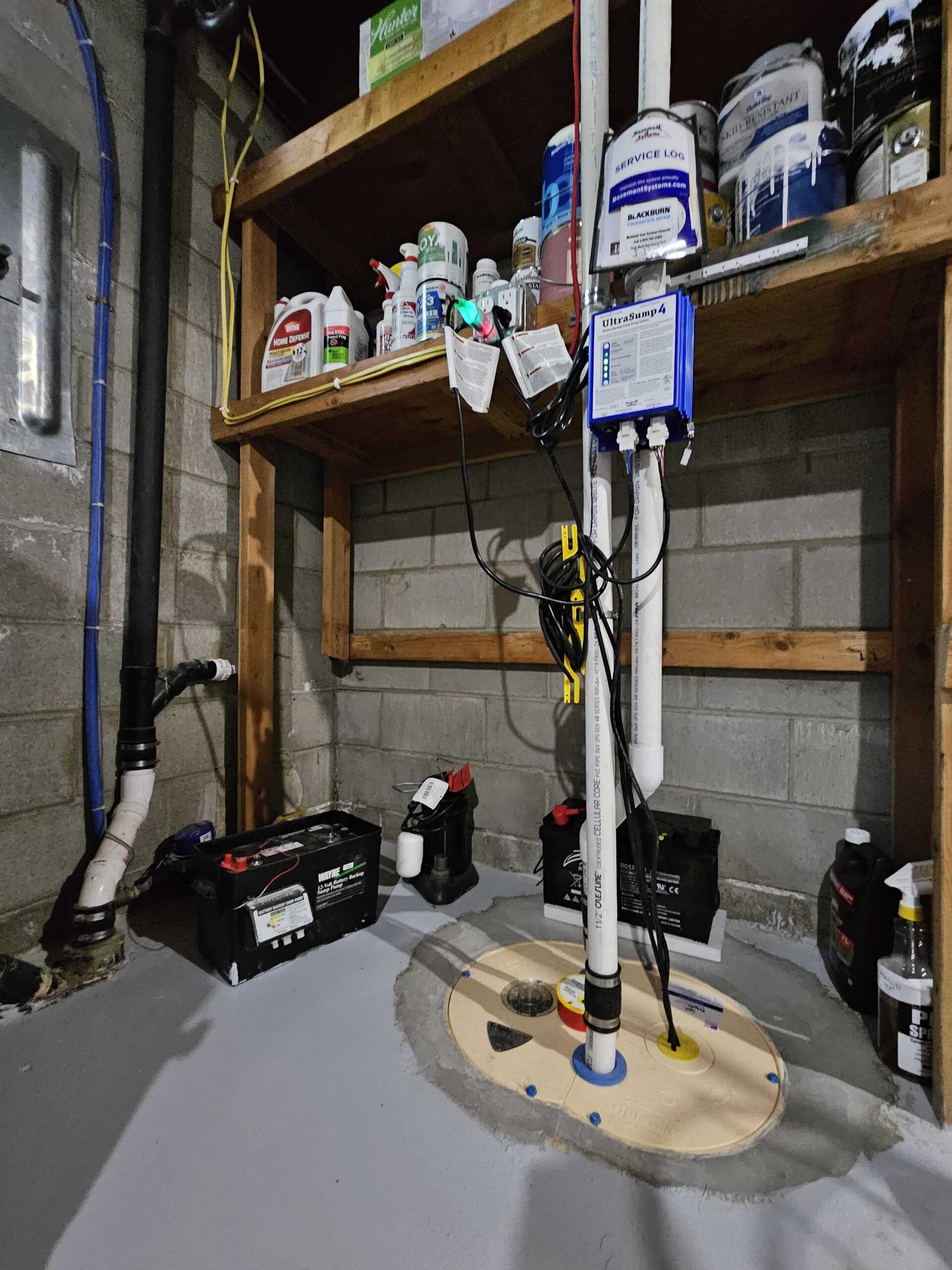 Basement sump pump system with a covered basin, discharge piping, and battery backup equipment.