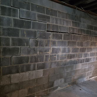 Basement concrete block wall with horizontal and stair-step cracking before wall anchor installation.